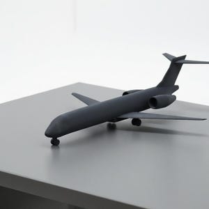 May include: A dark gray model airplane with wings, tail fins, and two engines. The toy airplane is resting on a gray surface, with a white background. The model is a detailed replica of a passenger jet.