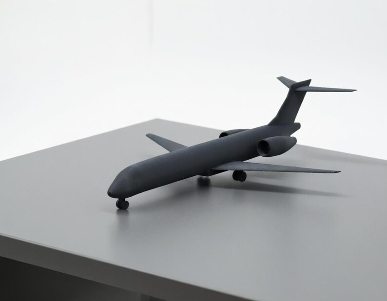 May include: A dark gray model airplane with wings, tail fins, and two engines. The toy airplane is resting on a gray surface, with a white background. The model is a detailed replica of a passenger jet.