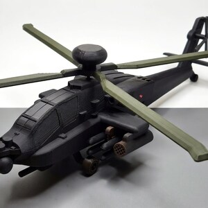 May include: A detailed model of a black helicopter with olive green rotor blades. The model features intricate detailing, including the cockpit, weapons, and tail rotor. The helicopter is positioned on a gray surface.