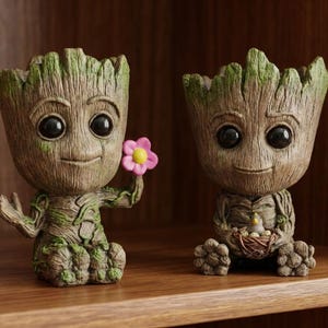 Puede incluir: Dos figuras de Groot, una sosteniendo una flor rosa y amarilla, la otra acunando un pájaro en un nido. Las figuras son marrones con acentos verdes y tienen ojos grandes y expresivos. Se exhiben en una estantería de madera.