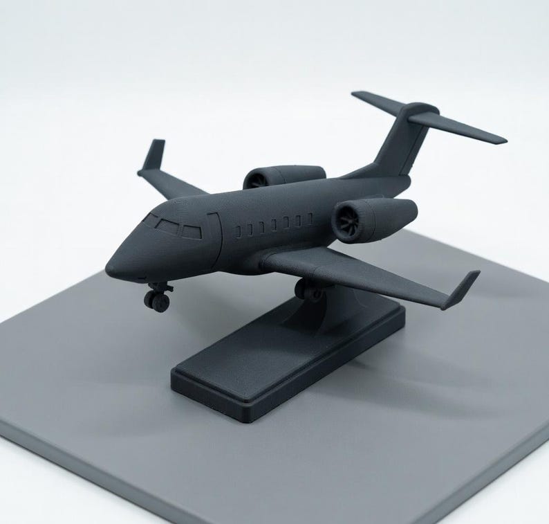 May include: A matte black model airplane, a miniature replica of a jet, is displayed on a gray rectangular base. The model features detailed wings, engines, and a cockpit, showcasing a sleek, modern design. The airplane is a decorative item.