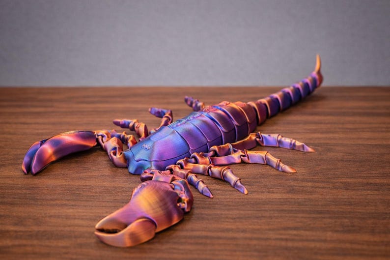 May include: A detailed, iridescent scorpion sculpture in shades of purple, blue, and gold. The arthropod has a segmented body, pincers, and a curved tail. The sculpture is displayed on a wooden surface.