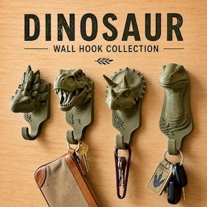 May include: Four olive green wall hooks shaped like dinosaur heads, including an ankylosaurus, a T-Rex, a triceratops, and a long-necked dinosaur. The text DINOSAUR WALL HOOK COLLECTION is printed above. Keys and a wallet hang from the hooks.