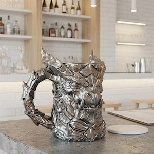 A professional collage showcasing over 20 unique 3D printable STL models for beer mugs and can holders. The image features high-detail designs including a horned Minotaur with gold accents, a gothic skull wearing aviator goggles, and a steampunk gas mask style tankard with copper pipes. The background displays various mythical, viking, and dark fantasy themed mugs in metallic silver and bronze finishes. Large yellow and blue 3D text in the center reads '20+ Can Holder & Beer Mug STL'.