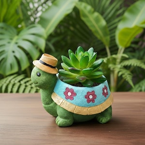 Könnte beinhalten: Ein grüner, schildkrötenförmiger Blumentopf mit kleinem Strohhut, der eine grüne Sukkulentenpflanze enthält. Der Topf hat einen blauen Rand mit roten Blumenmustern und einen gelben Rand.