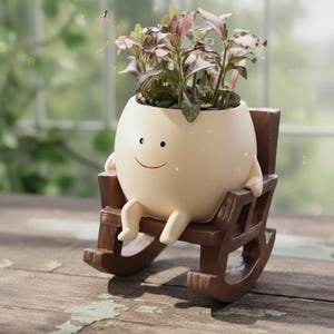 May include: A charming, cream-coloured egg-shaped planter with a smiling face, arms, and legs, sitting in a miniature brown rocking chair. The planter holds a vibrant green and pink plant, a delightful decorative item.