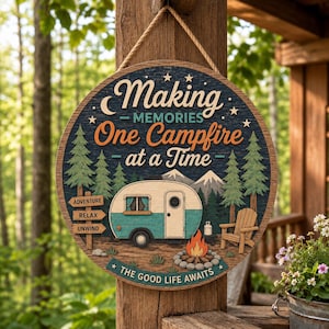 May include: A round wooden hanging sign featuring a teal and cream camper, a campfire, pine trees, and mountains. The text reads: Making Memories One Campfire at a Time, Adventure, Relax, Unwind, and The Good Life Awaits. It hangs from a rope.