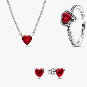May include: A jewellery set comprising a silver necklace, ring, and earrings. Each item features a heart-shaped, deep red gemstone. The ring is encircled by small, clear stones. The earrings are stud style.