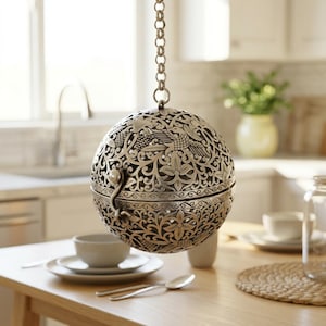 May include: A spherical, silver-toned metal hanging ornament featuring intricate cut-out patterns of birds and floral motifs. The hollow, two-piece orb is suspended by a matching metal chain, showcasing a detailed filigree design throughout.