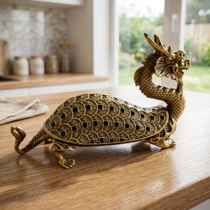 May include: A metallic gold-colored dragon turtle figurine featuring a detailed scaly neck and head. The shell is constructed from a repeating pattern of circular coin-like motifs with square cutouts, supported by four clawed feet and a curved tail.