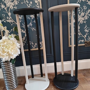May include: Two decorative plant stands. One stand has a black top and base with white legs, the other has a white top and base with black legs. The stands are round and have three legs each. The stands are made of wood.