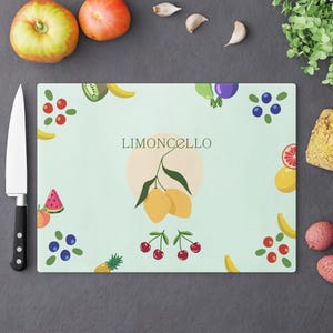 May include: A rectangular glass cutting board with a light green background featuring the text LIMONCELLO above a central illustration of two yellow lemons on a branch. The border is decorated with various colorful fruits including cherries, blueberries, watermelon slices, bananas, and pineapple.