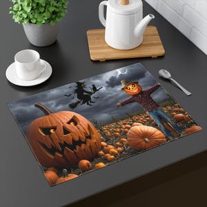 Peut inclure: Un set de table rectangulaire illustrant une scène d'Halloween avec une grande citrouille illuminée au premier plan, un épouvantail à tête de citrouille dans un champ et la silhouette d'une sorcière sur un balai sous un ciel sombre et nuageux.