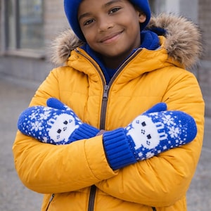 Könnte beinhalten: Ein Kind trägt einen leuchtend gelben Wintermantel mit einer fellgefütterten Kapuze und einer blauen Strickmütze. Das Kind trägt außerdem blaue Fäustlinge mit einem weißen Schneeflocken- und Bärenmuster. Das Kind hat die Arme verschränkt.