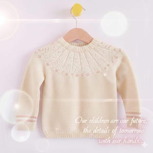 May include: Cream-colored children's sweater with a round neckline and long sleeves. The yoke features a detailed knit pattern with small pink accents. The sleeves have pink stripes near the cuffs. The text on the image reads: "Our children are our future, the details of tomorrow with our hands..."