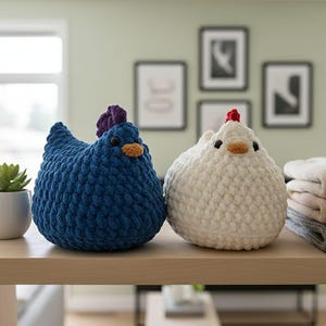 Può includere: Due figurine di gallina all'uncinetto fatte a mano, una blu e una bianca, sono affiancate su una mensola di legno. La gallina blu ha una cresta viola e la gallina bianca ha una cresta rossa. Entrambe hanno becchi arancioni e occhi neri.