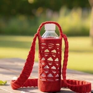 May include: A red crocheted water bottle holder with a strap, holding a clear plastic water bottle. The holder has a geometric openwork design. The bottle and holder are on a wooden table, with a blurred green background.