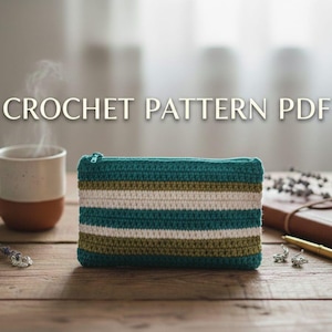 Può includere: Un astuccio all'uncinetto con un motivo a righe turchese, verde oliva e bianco. L'astuccio ha una cerniera turchese ed è esposto su una superficie di legno. Il testo "CROCHET PATTERN PDF" è nella parte superiore dell'immagine.