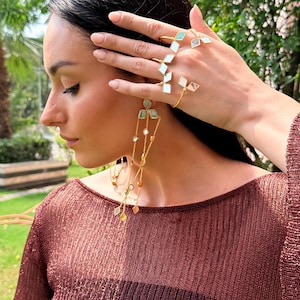 May include: Gold-toned jewelry set featuring a ring, bracelet, and earrings. The ring and bracelet have geometric designs with white and green accents. The earrings have a cascading design with various colored stones.