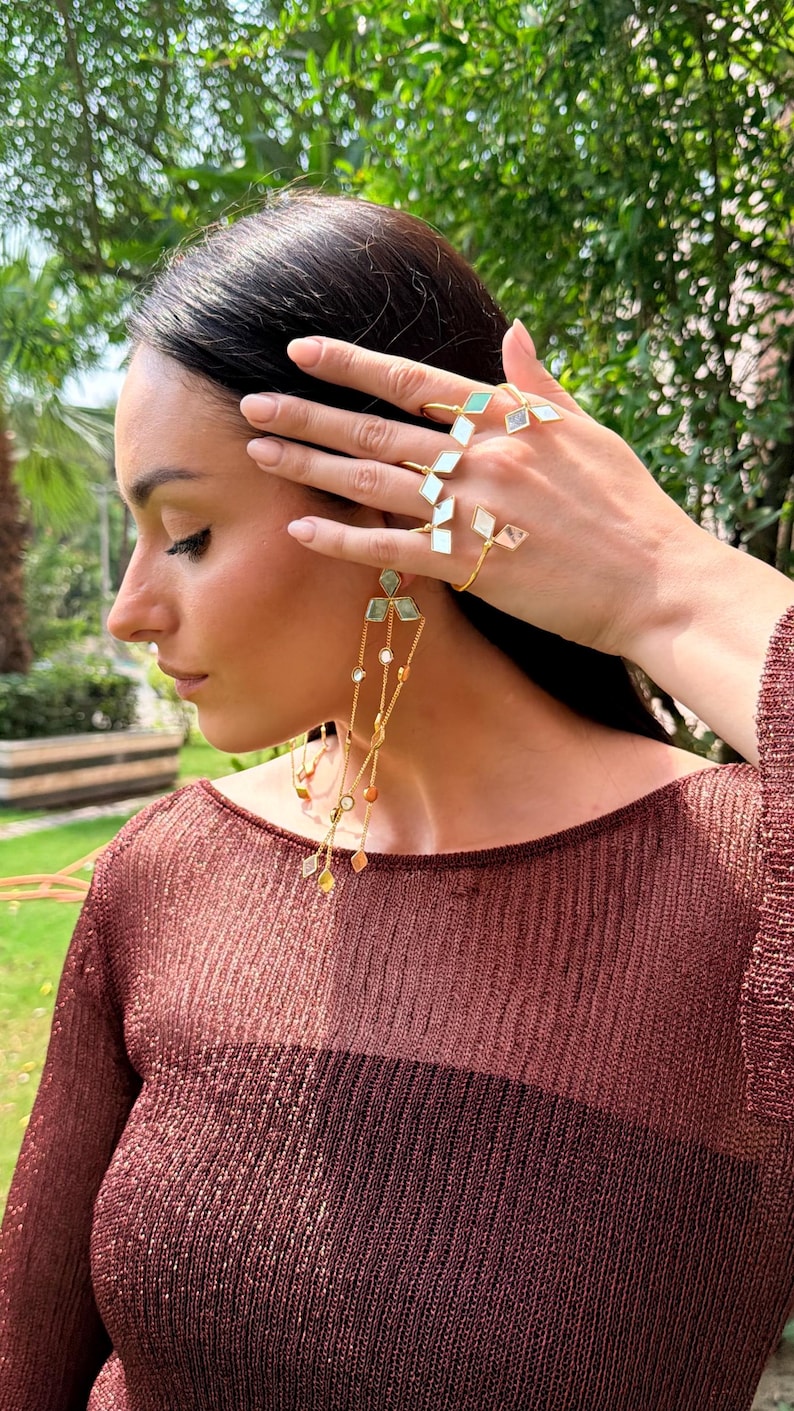 May include: Gold-toned jewelry set featuring a ring, bracelet, and earrings. The ring and bracelet have geometric designs with white and green accents. The earrings have a cascading design with various colored stones.