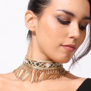 May include: Gold-toned choker necklace with mirrored accents and dangling fringe. The necklace features a geometric design with small, reflective squares and long, delicate gold strands. A stylish accessory.
