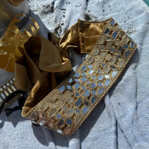 Woman wearing a handcrafted mirror work bandana with gold and turquoise embroidery
	2.	Side angle of embroidered headband under a beach umbrella, perfect for summer styling
	3.	Close-up of gold bangles and mirror work headband paired with chandelier earrings
	4.	Relaxing beach shot highlighting the statement mirror work headband and jewelry ensemble