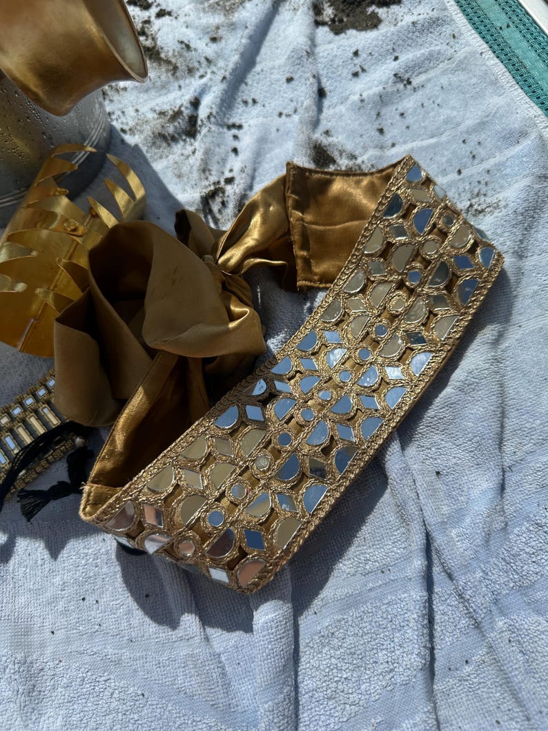 Woman wearing a handcrafted mirror work bandana with gold and turquoise embroidery
	2.	Side angle of embroidered headband under a beach umbrella, perfect for summer styling
	3.	Close-up of gold bangles and mirror work headband paired with chandelier earrings
	4.	Relaxing beach shot highlighting the statement mirror work headband and jewelry ensemble