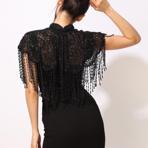 Model wearing a black embroidered beaded cape with scalloped edges and fringe. The sheer net base is hand-embellished with intricate embroidery and sparkling black beads, creating a statement bridal or evening accessory.