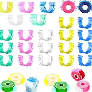 May include: A collection of U-shaped plastic bobbin clips in yellow, pink, blue, green, and clear, alongside several circular sewing machine bobbins wound with various colored threads including green, blue, yellow, red, and pink.