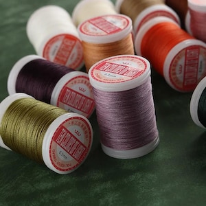 May include: A collection of polyester thread spools in various colors including olive green, lavender, dark purple, white, orange, and tan. Each spool features a white label with the text Ten Colors of Light and a 0.5mm thickness specification.