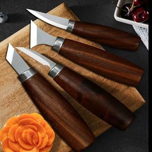 May include: A set of four wood carving knives with dark brown wooden handles and silver metal ferrules. The blades vary in shape, including pointed, flat, and angled tips. The knives are arranged on a light brown wooden cutting board.