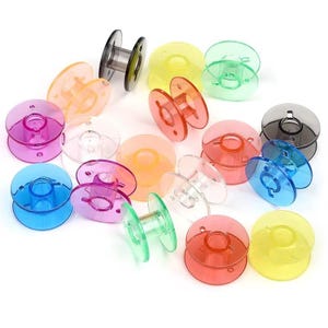 Pode incluir: Uma coleção de bobinas de máquina de costura de plástico translúcido em várias cores vibrantes, incluindo rosa, azul, laranja, amarelo, verde e transparente. Cada bobina apresenta um design circular com um núcleo central e pequenos furos.