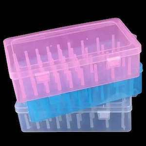May include: A stack of three rectangular plastic storage boxes with hinged lids and internal vertical pegs. The top box is translucent pink, the middle box is translucent blue, and the bottom box is clear. Each container features a secure latch.