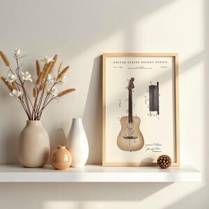 May include: A framed print of a guitar patent illustration. The print is in a light wood frame and features a detailed drawing of a guitar with technical diagrams. The print is displayed on a white shelf with vases and decorative elements.