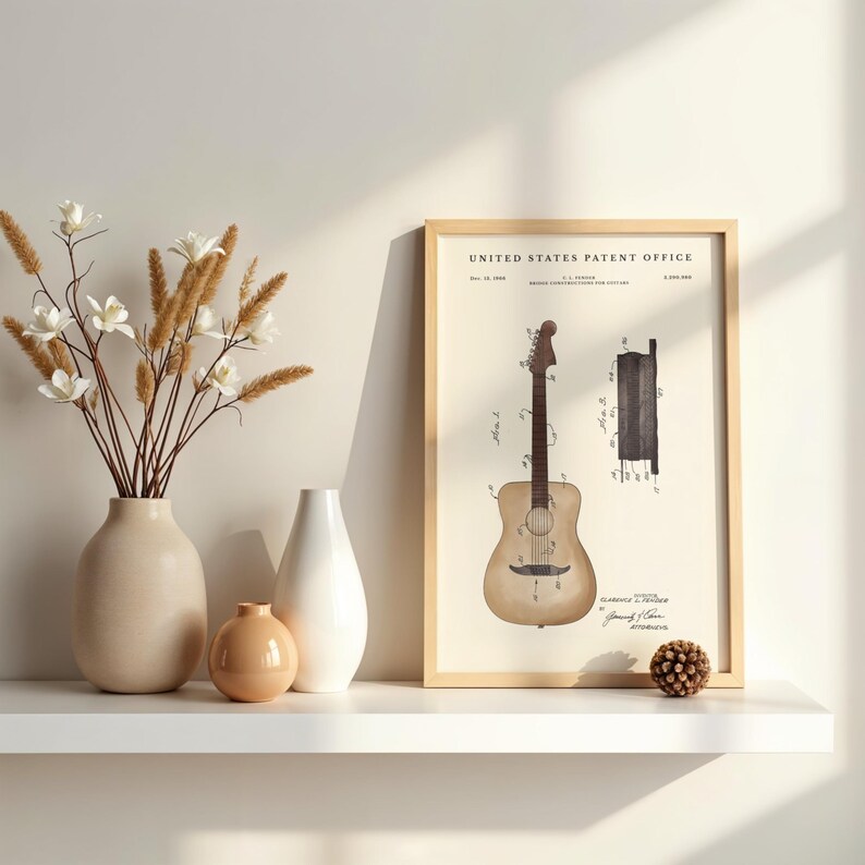 May include: A framed print of a guitar patent illustration. The print is in a light wood frame and features a detailed drawing of a guitar with technical diagrams. The print is displayed on a white shelf with vases and decorative elements.