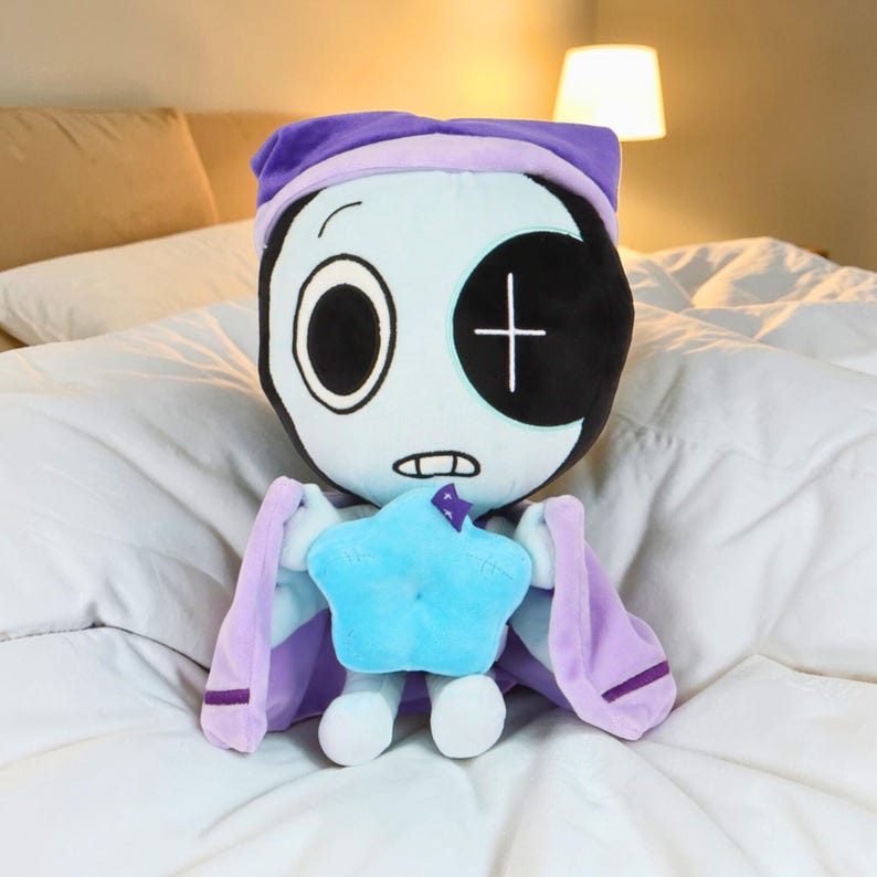 May include: A plush doll with a light blue face, black eye patch, and a purple nightcap. The doll has a blue star-shaped body and purple cape-like arms. The doll is sitting on a white bed.