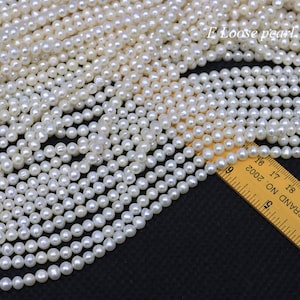 Puede incluir: Primer plano de una hebra de perlas blancas, con una regla que mide las perlas a aproximadamente 6 mm de diámetro. Las perlas son lisas y redondas, y están dispuestas en una pila suelta.