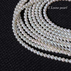 Puede incluir: Múltiples hilos de pequeñas perlas blancas y redondas. Las perlas están ensartadas, creando varias filas. El texto "E Loose pearl" es visible. El fondo es una superficie oscura y texturizada.