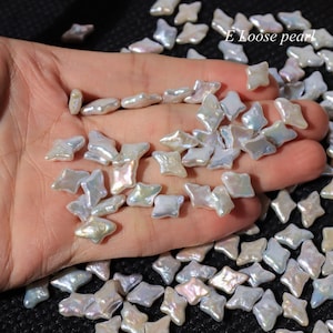 Puede incluir: Perlas sueltas iridiscentes en forma de estrella. Las perlas tienen un brillo nacarado con toques de azul, rosa y amarillo. Las perlas están dispersas sobre una superficie, algunas descansando en una mano. El texto "E Loose pearl" es visible.