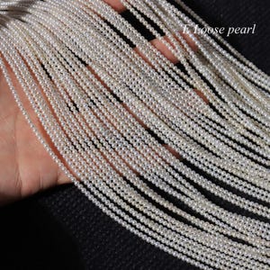 Peut inclure: Plusieurs brins de petites perles blanches. Les perles sont enfilées ensemble, créant de nombreuses lignes de perles délicates et lumineuses. L'image est bien éclairée, soulignant la texture lisse et la forme ronde des perles. Le texte de l'image indique "E Loose pearl".