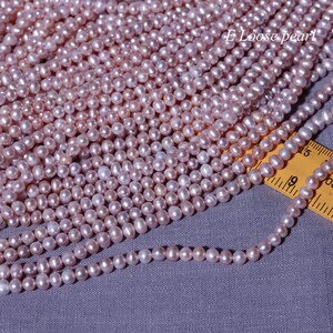 May include: A strand of pale pink freshwater pearls, approximately 4mm in diameter, displayed on a grey fabric surface with a yellow measuring tape. The pearls are loose and ready to be used for jewellery making.
