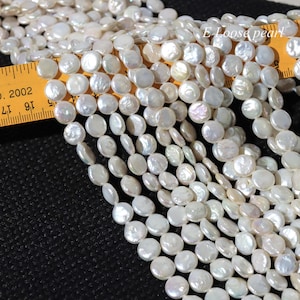 May include: A close-up shot of a collection of white, flat, disc-shaped pearls. The pearls are strung together, creating a flowing, organic texture. A yellow ruler is partially visible, providing scale. The text "E Loose pearl" is in the upper right corner.
