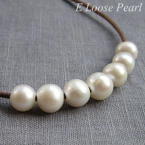 May include: A necklace made of white pearls strung on a brown leather cord. The pearls are round and smooth, and the cord is thin and delicate.