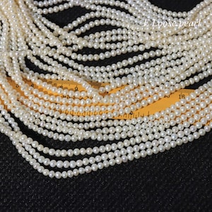 May include: Multiple strands of small, white pearls are displayed. The pearls are round and have a shiny surface. The text "E Loose pearl" is visible. A yellow ruler is in the background, with measurements in centimetres.