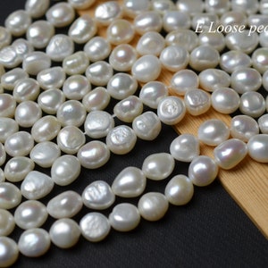 Puede incluir: Una hebra de perlas blancas sueltas, con una forma ligeramente irregular, dispuestas en una fila sobre una superficie de madera. Las perlas son lisas y lustrosas, con un sutil brillo iridiscente. El texto "E Loose pearl" es visible en la esquina superior derecha de la imagen.