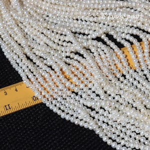 Könnte beinhalten: Nahaufnahme einer weißen Süßwasserperlenkette. Die Perlen sind klein und rund und in einer Reihe angeordnet. Ein Lineal ist im Bild sichtbar und zeigt die Größe der Perlen an.