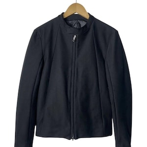 May include: A black jacket with a stand-up collar and a full-length zipper. The jacket is hanging on a wooden hanger. The jacket's design is simple and streamlined, with a tailored fit. The fabric appears to be a smooth, solid color.