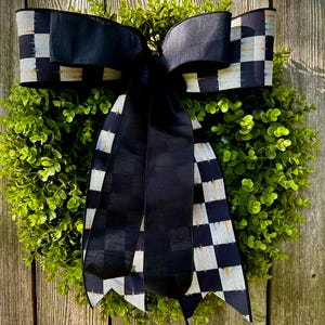 May include: A round green wreath with a large black bow featuring a checkered pattern in black and white. The wreath is set against a weathered wooden background, creating a rustic and elegant aesthetic.