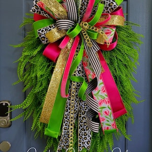 May include: A decorative wreath with a vibrant mix of ribbons in gold, hot pink, green, and black and white patterns, including leopard print and stripes. The wreath has a base of green foliage and the text "God Given Gifts".