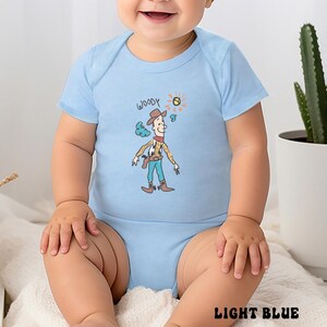 May include: Light blue baby bodysuit featuring a cartoon illustration of Woody from Toy Story. The design includes Woody's hat, vest, and boots, with the name "Woody" above the character. The words "Light Blue" are printed at the bottom.